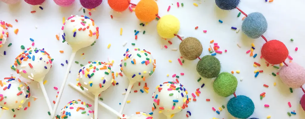 Funfetti cake pops with sprinkles next to rainbow ball garland